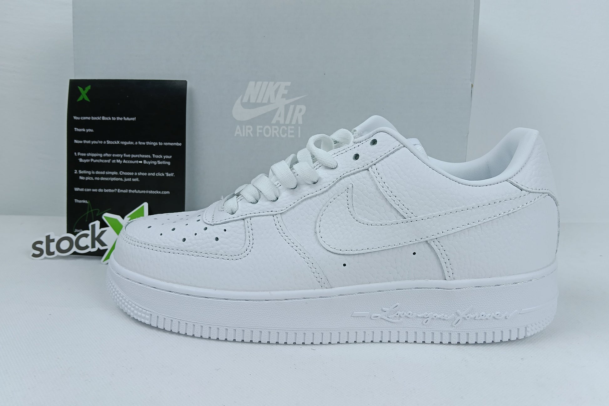 White Nike Air Force sneakers with a box and 'stockx' label in the background